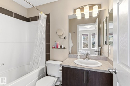 Bathroom featuring a white tub and shower combination, dark brown wall tiling, a vanity with dark wood-finish cabinetry, a light-toned countertop, and a large mirror with integrated lighting - 7114 22 Avenue, Edmonton, AB - Indoor Photo Showing Bathroom
