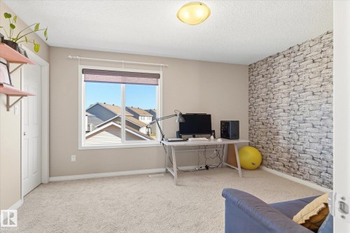 Carpeted room featuring a large window, neutral wall paint, and a stone-effect accent wall - 7114 22 Avenue, Edmonton, AB - Indoor