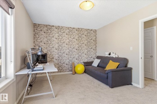 Carpeted room featuring a stone-patterned accent wall, a window with a roller shade, and a flush-mount ceiling light - 7114 22 Avenue, Edmonton, AB - Indoor