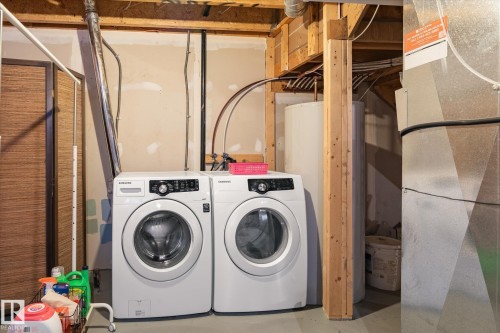 Dedicated laundry area featuring a front-loading washer and dryer, utility sink, exposed ceiling joists, and a water heater - 7114 22 Avenue, Edmonton, AB - Indoor Photo Showing Laundry Room
