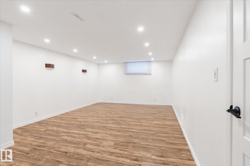 The property features a spacious room with light wood-tone flooring, recessed lighting, and white walls - 12823 81 Street, Edmonton, AB - Indoor
