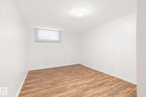 Spacious room featuring light wood-look flooring, white walls, and a window with a roller blind - 12823 81 Street, Edmonton, AB - Indoor Photo Showing Other Room