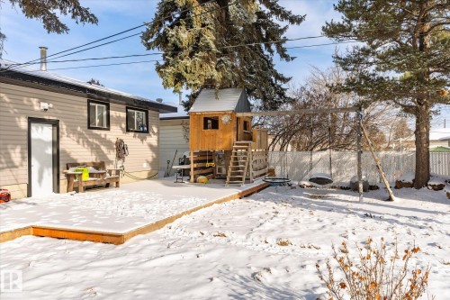 The property features a spacious backyard with a wooden deck, a play structure, and mature trees - 12823 81 Street, Edmonton, AB - Outdoor