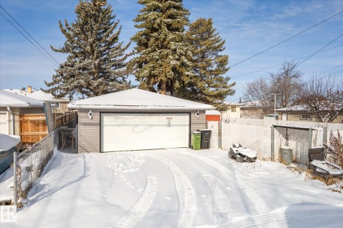 Detached garage featuring a white garage door, light grey siding, and exterior lighting fixtures - 12823 81 Street, Edmonton, AB - Outdoor