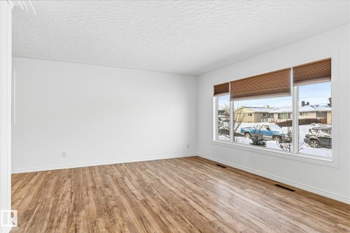 This room features light-toned wood flooring, white walls, and a large window with three panes and privacy blinds - 12823 81 Street, Edmonton, AB - Indoor