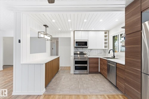The kitchen features a blend of white and wood-toned cabinetry, stainless steel appliances, and a window above the sink - 12823 81 Street, Edmonton, AB - Indoor Photo Showing Kitchen