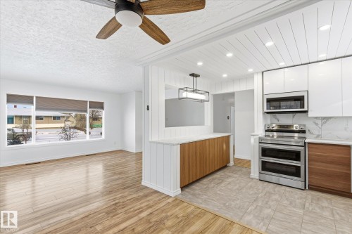 The property features an open-concept living area with large windows, wood-look flooring, and a ceiling fan - 12823 81 Street, Edmonton, AB - Indoor Photo Showing Kitchen