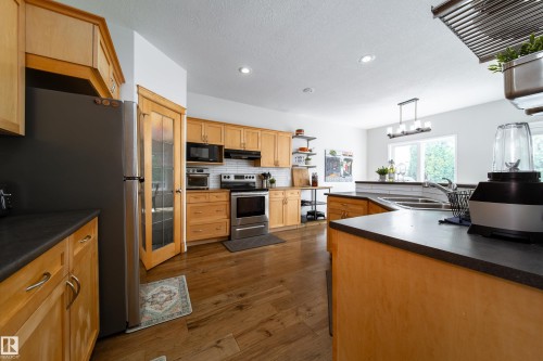 Open-concept kitchen featuring wood-finish flooring, ample cabinetry, and dark countertops - 1205 Ormsby Lane, Edmonton, AB - Indoor Photo Showing Kitchen With Stainless Steel Kitchen With Double Sink