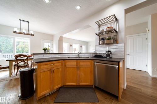 Open-concept kitchen with wood-finish flooring, light wood cabinetry, and a stainless steel dishwasher - 1205 Ormsby Lane, Edmonton, AB - Indoor Photo Showing Kitchen With Double Sink