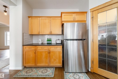 Kitchenette featuring light wood-finish cabinetry, a stainless steel refrigerator, dark countertops, and a white subway tile backsplash - 1205 Ormsby Lane, Edmonton, AB - Indoor Photo Showing Kitchen