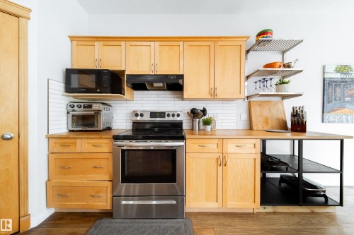 Kitchen featuring wood-finish cabinetry, stainless steel appliances, a white subway tile backsplash, butcher block countertops, and open shelving - 1205 Ormsby Lane, Edmonton, AB - Indoor Photo Showing Kitchen