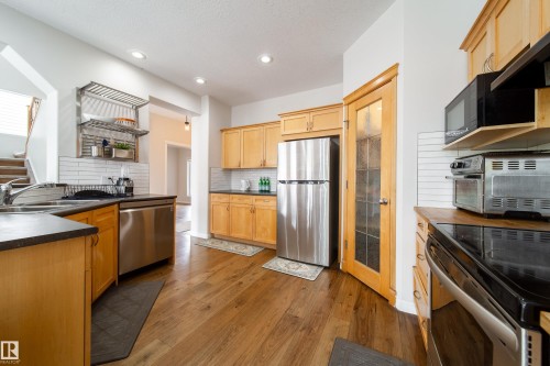 Kitchen featuring wood-finish flooring, light wood cabinetry, stainless steel appliances, dark countertops, and white subway tile backsplash - 1205 Ormsby Lane, Edmonton, AB - Indoor Photo Showing Kitchen With Stainless Steel Kitchen With Double Sink