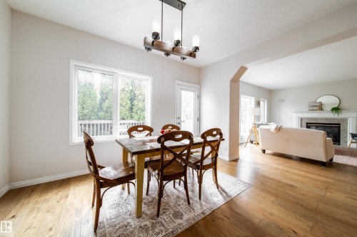 Open-concept living area featuring wood-finish flooring throughout, a dining space with a large window, and an arched doorway opening to the living room with a fireplace - 1205 Ormsby Lane, Edmonton, AB - Indoor Photo Showing Dining Room