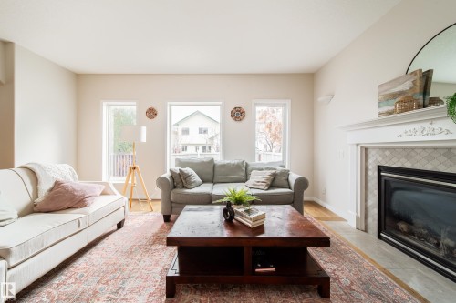Living area featuring multiple windows providing natural light, a fireplace with a decorative mantel and patterned tile surround, and wood-finish flooring - 1205 Ormsby Lane, Edmonton, AB - Indoor Photo Showing Living Room With Fireplace