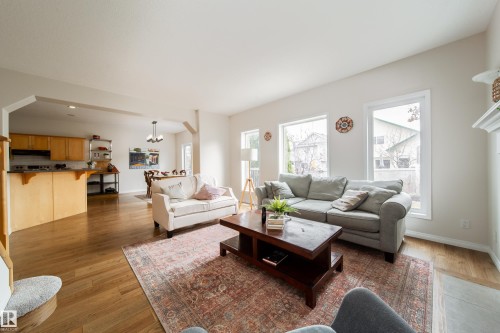 Open-concept living area featuring wood-finish flooring, multiple windows, a white mantel, and a kitchen pass-through - 1205 Ormsby Lane, Edmonton, AB - Indoor Photo Showing Living Room