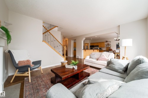 Open-concept living area featuring a fireplace mantel, staircase with wood handrail and metal balusters, and wood-finish flooring - 1205 Ormsby Lane, Edmonton, AB - Indoor Photo Showing Living Room