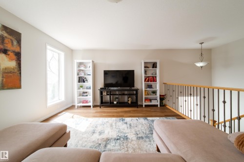 Bright living area featuring wood-finish flooring, a decorative window, and a wood railing with wrought iron balusters - 1205 Ormsby Lane, Edmonton, AB - Indoor Photo Showing Living Room