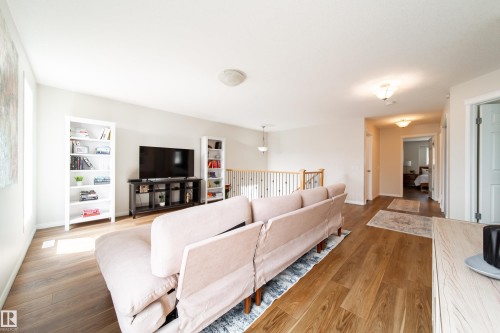 Spacious living area featuring wood-finish flooring, light neutral wall tones, and a wooden staircase with black iron balusters - 1205 Ormsby Lane, Edmonton, AB - Indoor Photo Showing Living Room