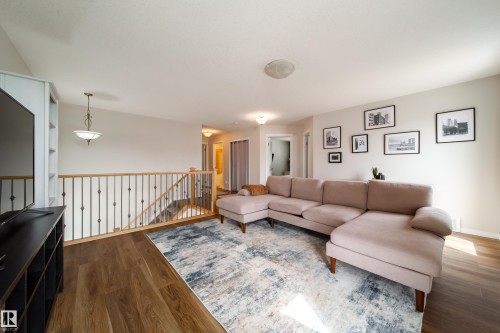 Open upper-level area featuring wood-finish flooring, a contemporary railing with black metal balusters, and light-toned wall finishes - 1205 Ormsby Lane, Edmonton, AB - Indoor Photo Showing Living Room