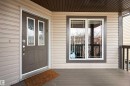 Inviting front entry featuring a brown paneled door with decorative glass inserts, light beige horizontal siding, a white-framed window with grilles, and a wood-finish porch floor - 1205 Ormsby Lane, Edmonton, AB  - Outdoor With Deck Patio Veranda With Exterior 