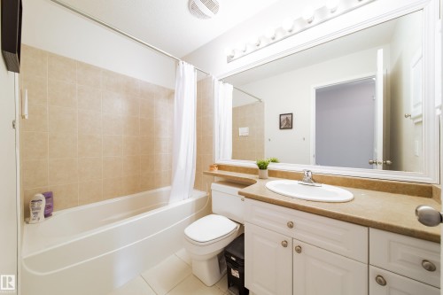 Full bathroom featuring a white vanity with an integrated sink, a large mirror, and a full bathtub with beige wall tiling - 1205 Ormsby Lane, Edmonton, AB - Indoor Photo Showing Bathroom