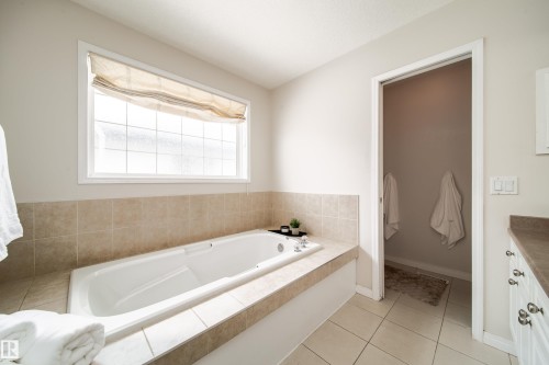 Soaking tub with a tiled surround, frosted window, and light-toned tile flooring - 1205 Ormsby Lane, Edmonton, AB - Indoor Photo Showing Bathroom