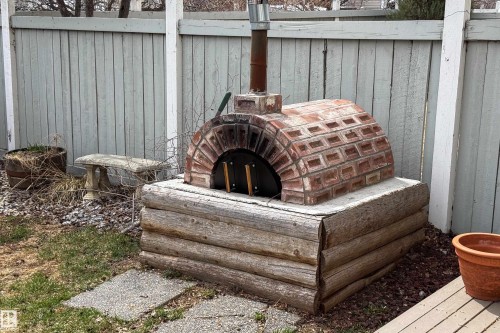 Outdoor brick pizza oven with a metal flue, supported by a rustic log base - 1205 Ormsby Lane, Edmonton, AB - Outdoor With Exterior