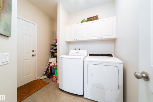 Dedicated laundry area featuring white upper cabinetry, tiled flooring, and a solid white door with brushed nickel hardware - 1205 Ormsby Lane, Edmonton, AB - Indoor Photo Showing Laundry Room