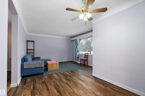 This living area features rich hardwood flooring, a ceiling fan with integrated lighting, and a large window providing natural light - 7720 85 Avenue, Edmonton, AB - Indoor Photo Showing Other Room