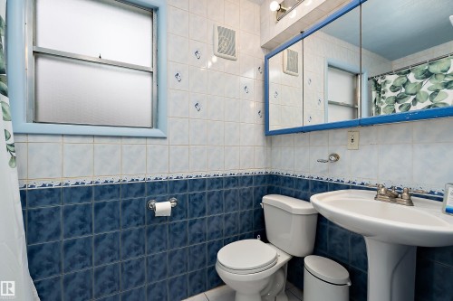 Bathroom featuring blue and white tiled walls, a window, and a wall-mounted mirrored cabinet - 7720 85 Avenue, Edmonton, AB - Indoor Photo Showing Bathroom