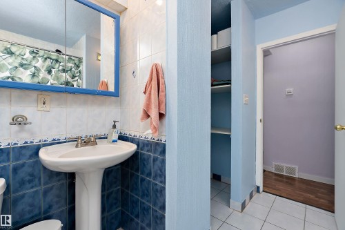 Bathroom featuring a pedestal sink, a wall-mounted medicine cabinet with a blue frame, and tiled walls in white and blue - 7720 85 Avenue, Edmonton, AB - Indoor Photo Showing Bathroom