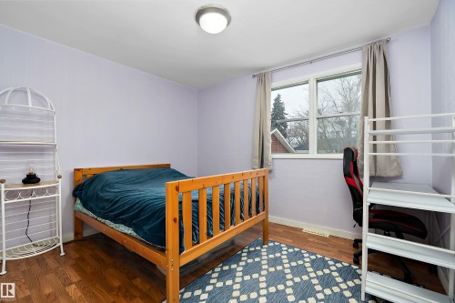This room features hardwood flooring, light purple walls, and a window providing natural light - 7720 85 Avenue, Edmonton, AB - Indoor Photo Showing Bedroom