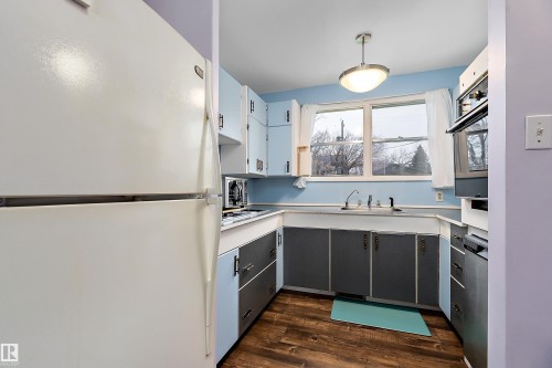 The kitchen features light wood-look flooring, light blue and dark gray cabinetry, and a window above the sink - 7720 85 Avenue, Edmonton, AB - Indoor Photo Showing Kitchen