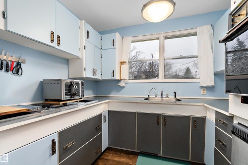 This kitchen features light blue upper cabinetry and dark gray lower cabinetry with white countertops - 7720 85 Avenue, Edmonton, AB - Indoor Photo Showing Kitchen