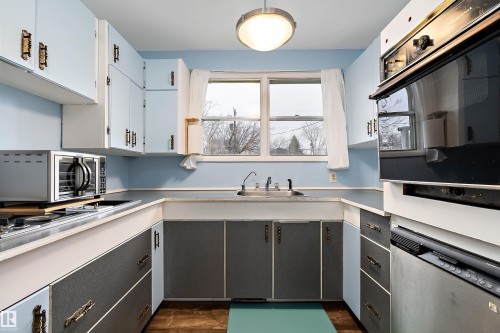 The kitchen features light blue upper cabinetry with decorative hardware, a double-basin sink, and an integrated wall oven - 7720 85 Avenue, Edmonton, AB - Indoor Photo Showing Kitchen