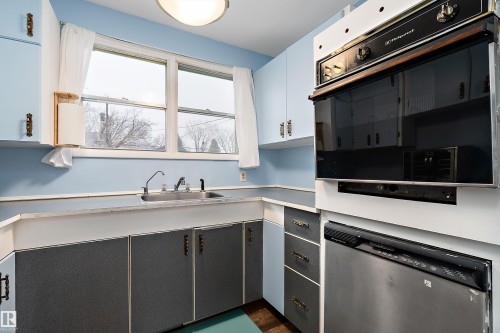 The kitchen features a double basin stainless steel sink, light blue wall cabinets, and a built-in oven and dishwasher - 7720 85 Avenue, Edmonton, AB - Indoor Photo Showing Kitchen