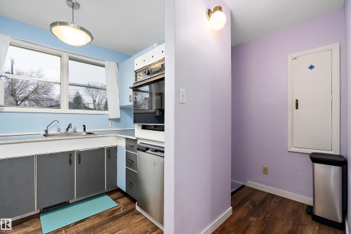 The kitchen features a sink beneath a window, built-in oven, and wood-look flooring - 7720 85 Avenue, Edmonton, AB - Indoor Photo Showing Kitchen