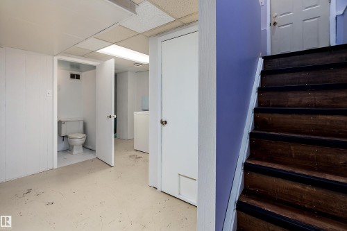 The property features a finished basement area with a toilet, laundry appliances, and a staircase with wooden treads - 7720 85 Avenue, Edmonton, AB - Indoor Photo Showing Other Room