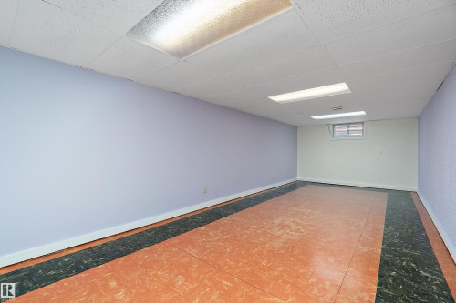 Spacious room featuring a drop ceiling with fluorescent lighting, light purple and white walls, and a tiled floor with a central orange section and dark perimeter - 7720 85 Avenue, Edmonton, AB - Indoor