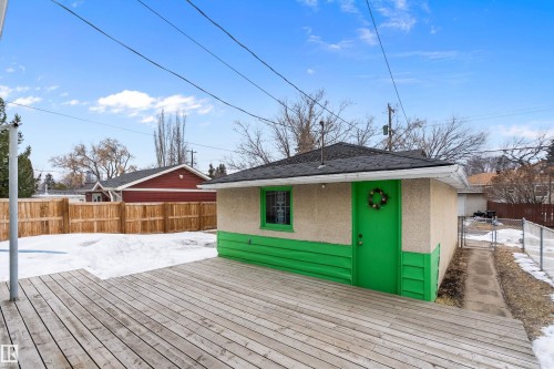 The property features a spacious wooden deck and an exterior building with a bright green door and trim - 7720 85 Avenue, Edmonton, AB - Outdoor With Deck Patio Veranda
