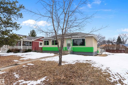 The property features a concrete walkway leading to the front entrance, a front yard with remnants of snow and leaves, and a light-colored exterior with green accents - 7720 85 Avenue, Edmonton, AB - Outdoor