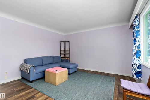 This inviting room features hardwood style flooring, light purple walls, and a window with colorful curtains - 7720 85 Avenue, Edmonton, AB - Indoor Photo Showing Other Room