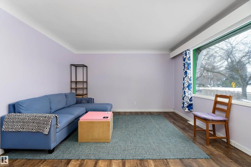 The living area features wood-style flooring, a large window, and a light-colored rug - 7720 85 Avenue, Edmonton, AB - Indoor