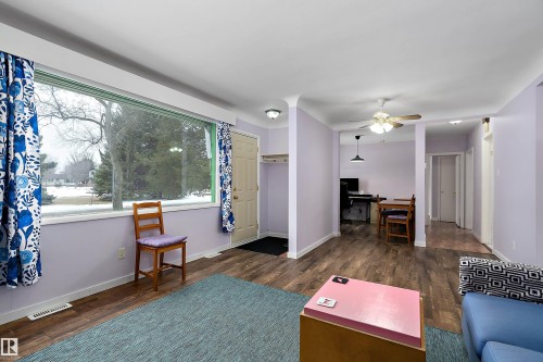 This living area features a large window with blue and white patterned curtains, wood-look flooring, and light purple walls - 7720 85 Avenue, Edmonton, AB - Indoor