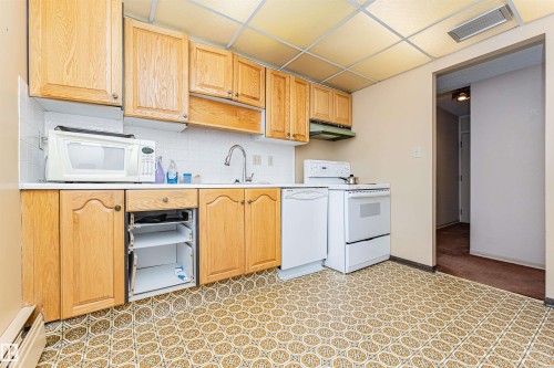 Kitchen featuring wood cabinetry, white appliances, patterned flooring, and a drop ceiling with recessed lighting - 407 10045 118 Street, Edmonton, AB - Indoor Photo Showing Kitchen