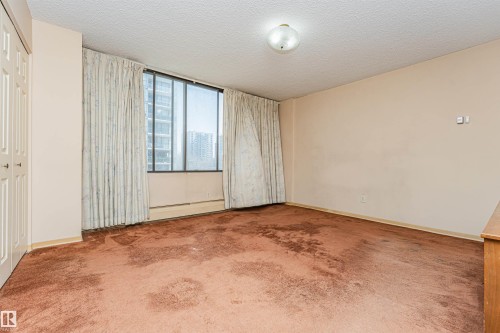 Spacious room with a large window, textured ceiling, wall-to-wall carpeting, and baseboard heating - 407 10045 118 Street, Edmonton, AB - Indoor Photo Showing Other Room
