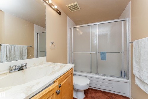 Bathroom featuring a wood vanity with a single basin sink, a large wall-mounted mirror, and a shower-tub combination with sliding frosted glass doors - 407 10045 118 Street, Edmonton, AB - Indoor Photo Showing Bathroom