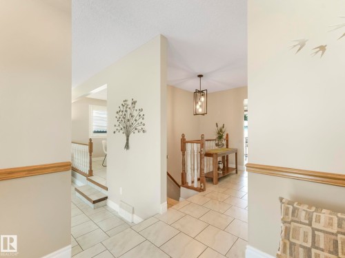 Tiled entryway featuring a modern three-light pendant fixture, wood handrails, and a multi-level design - 1027 77 Street, Edmonton, AB - Indoor Photo Showing Other Room