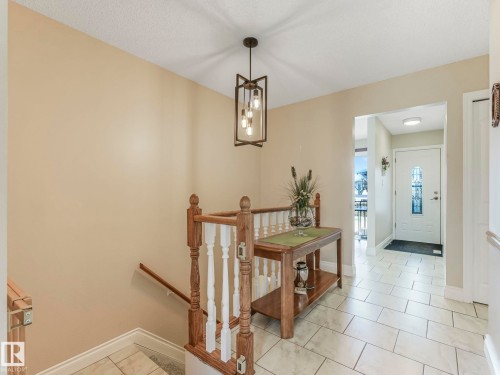 Foyer featuring a white entry door with decorative glass, light-toned rectangular tile flooring, and a contemporary multi-bulb ceiling light fixture - 1027 77 Street, Edmonton, AB - Indoor Photo Showing Other Room