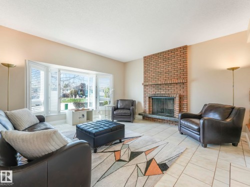Living area featuring a brick fireplace, a prominent bay window with white plantation shutters, and light-toned tile flooring - 1027 77 Street, Edmonton, AB - Indoor Photo Showing Living Room With Fireplace